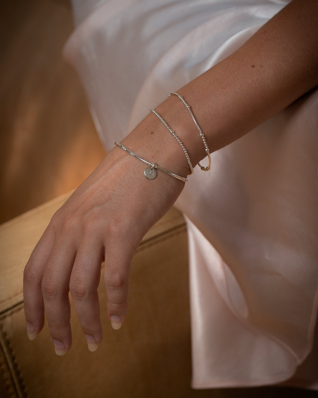 Close up of layered sterling silver bracelet stack with bead and bar bracelets and letter charm
