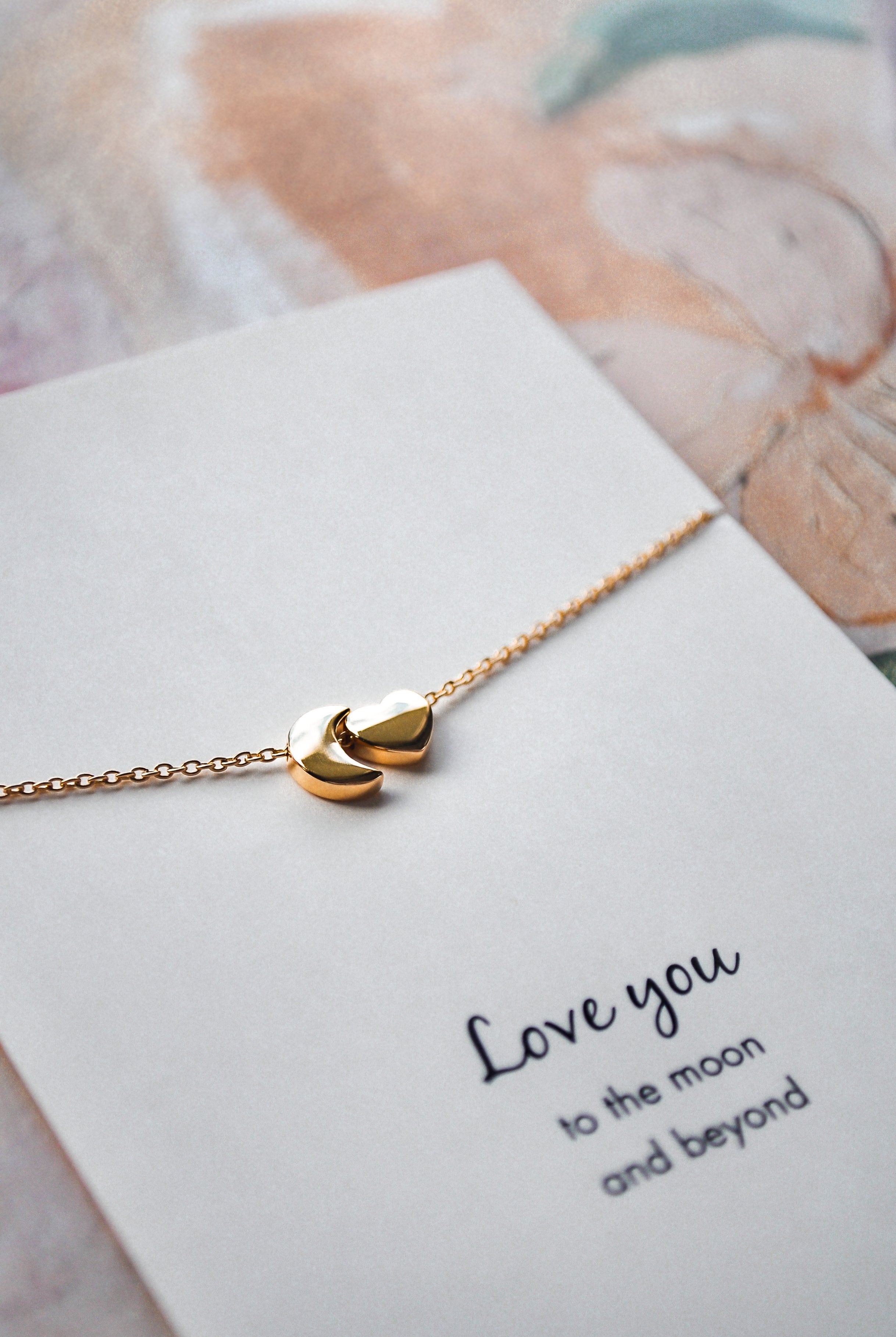 Close up of gold chain detail with moon and heart pendant